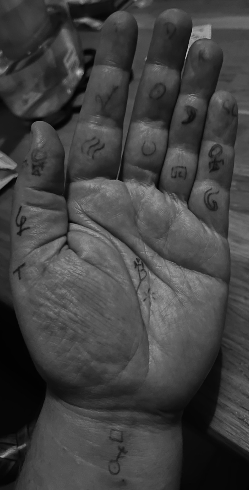 A black and white photograph of an open palm and fingers, covered in hand-drawn ink symbols.
